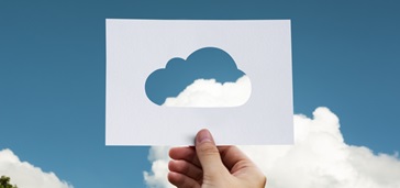 paper cutout of a cloud shape held against clouds