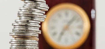 stack of coins with out of focus clock in the background