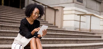 woman sitting on steps of building, looking at smart device