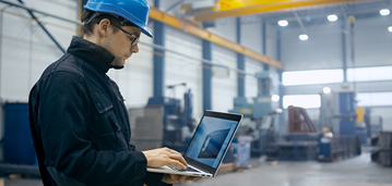 man wearing hardhat in factory holding laptop