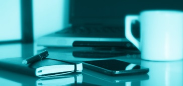 notebook, smartphone, and coffeecup on table; blue-green tint over entire image