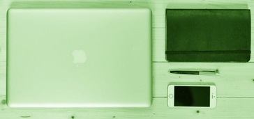 overhead shot of laptop, smartphone, notebook, and pen on table, green tint