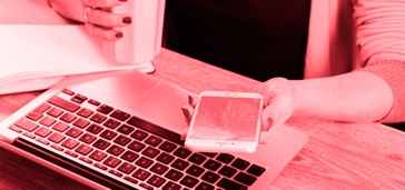 woman's hands holding smartphone and drink over laptop, pink tint